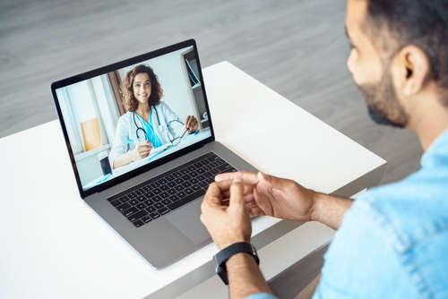 View over male client shoulder sit at desk receive medical consultation online from female doctor. Indian man listening practitioner. Distant communication_ health protection and telemedicine concept