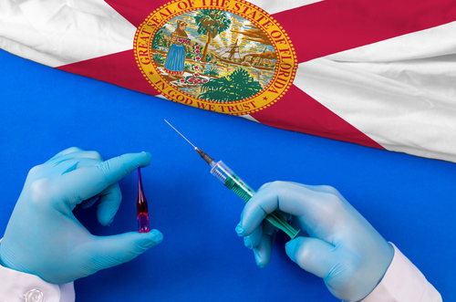 Florida Vaccination. Hands of doctor holding syringe and coronavirus  COVID-19  vial vaccine on flag Florida