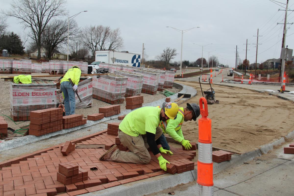 Workers lay brick pavers in the median of the 167th Street roundabouts near U.S. 69.