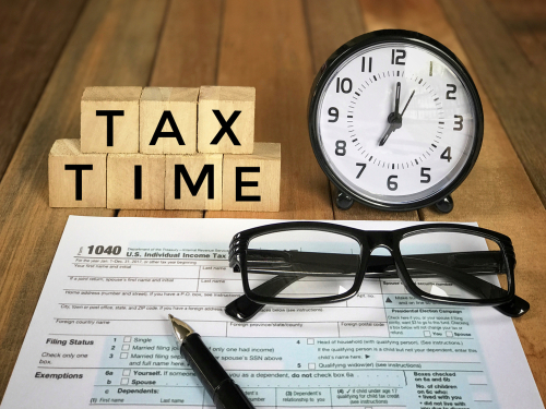 Tax-filling concept -  Tax time  words on wooden blocks_ pen_ eyeglasses_ featuring half of U.S IRS 1040 form. With vintage-styled background.
