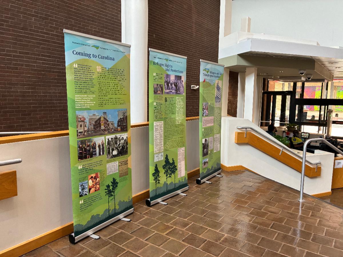 Three vertical banners with photos and text on each set up in the lobby of a building.