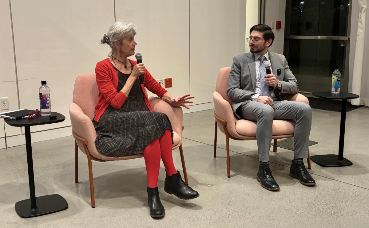 A woman and man sit in chairs side by side, speaking into microphones.