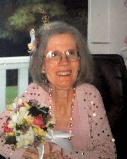 Pictured is the late Diane Coleman with glasses, wearing a peach dress and holding a bouquet of flowers. 