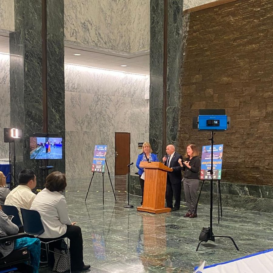 Image of NYS Legislative Day speakers at the podium standing and speaking to a group at the WELL of the NYS legislative building