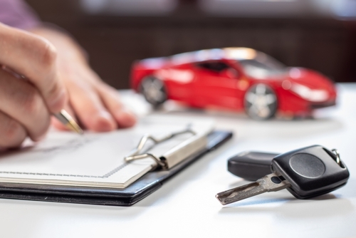 Man signing car insurance document or lease paper. Writing signature on contract or agreement. Buying or selling new or used vehicle. Car keys on table on red car background. Warranty or guarantee.