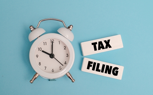 A coloured wooden block with text TAX FILING  on it next to white alarm clock