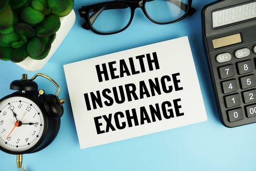 Health insurance exchange text on paper card with alarm clock and calculator top view on blue background