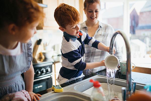 Children washing dishes in sink as parent looks on