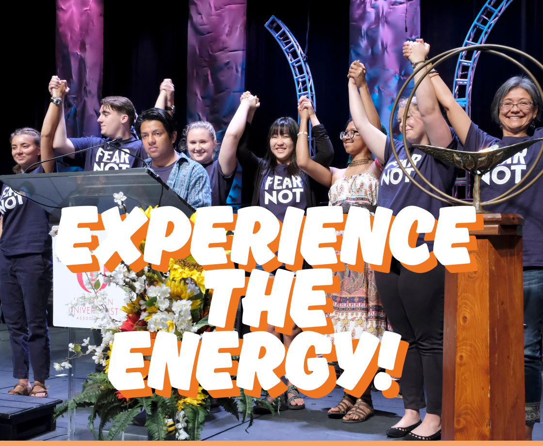 A diverse group of young people standing on a stage, holding hands raised in celebration. Most are wearing matching dark shirts with the words 'FEAR NOT.' Behind them are colorful stage lights and abstract structures. Large, bold text in the foreground reads 'EXPERIENCE THE ENERGY!' with an orange shadow effect. A bouquet of bright flowers is placed at the front of the stage near a podium.
