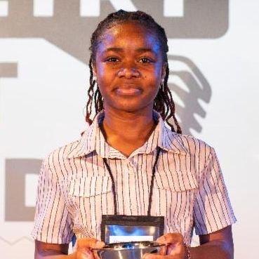 A young woman with dark skin and a white collared t-shirt holds a trophy