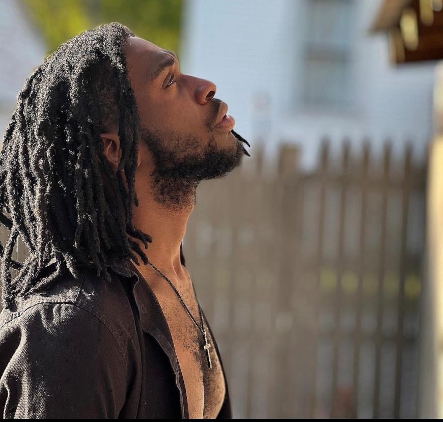 an outdoors headshot of a person with long brown hair and a beard looking to the sky