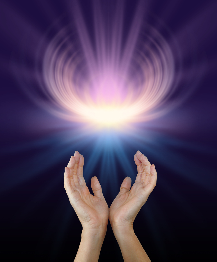 Female hands reaching up towards a glowing energy manifestation shaped like a lotus flower in pink and yellow with plenty of copy space