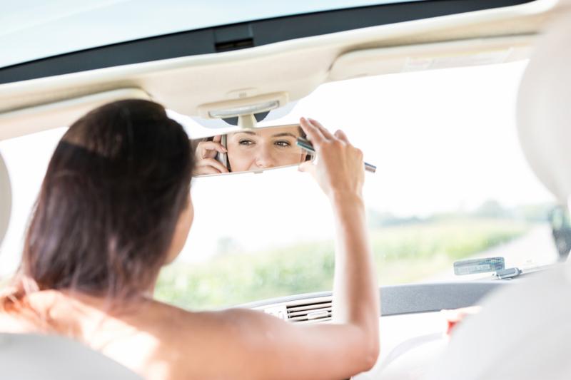 Woman adjusting rearview mirror while using mobile phone in car