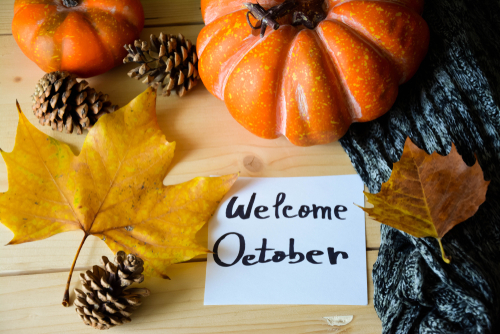 A note with Welcome October text on a rustic wooden table with Autumn de...