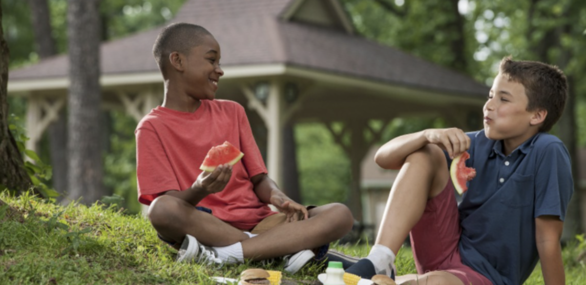 Two students are sitting on the grass, laughing and smiling