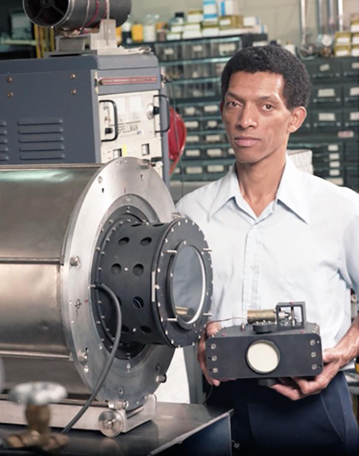 George Carruthers poses with astronomical equipment in a laboratory.