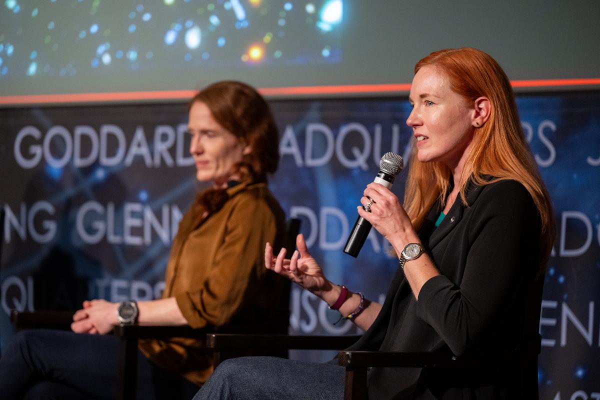 Amber Strahn speaks into a microphone on stage at the Hubble Symposium. Beside her is Julia Roman-Duval.