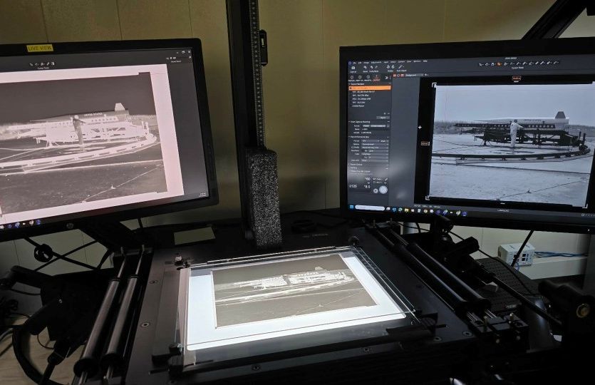 A scanner with a large-format negative on its bed has two monitors on either side, one showing the negative image, and the other the positive.