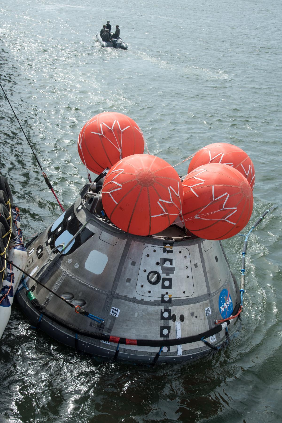 View from above of the Orion Crew Module floating in the ocean. It has 4 red inflated flotation bags at the top of the spacecraft. 