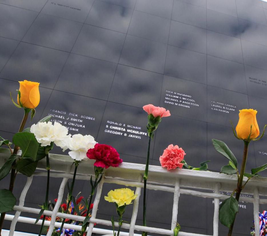 Flowers are affixed to a fence in front of the Space Mirror Memorial at the Kennedy Space Center Visitor Complex in Florida during NASA’s Day of Remembrance in 2023. 