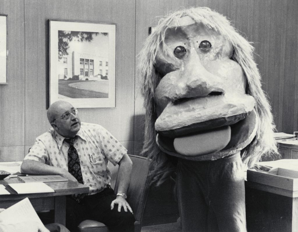 Clarence Syvertson sits at his desk and looks apprehensively at a giant creature in his office.