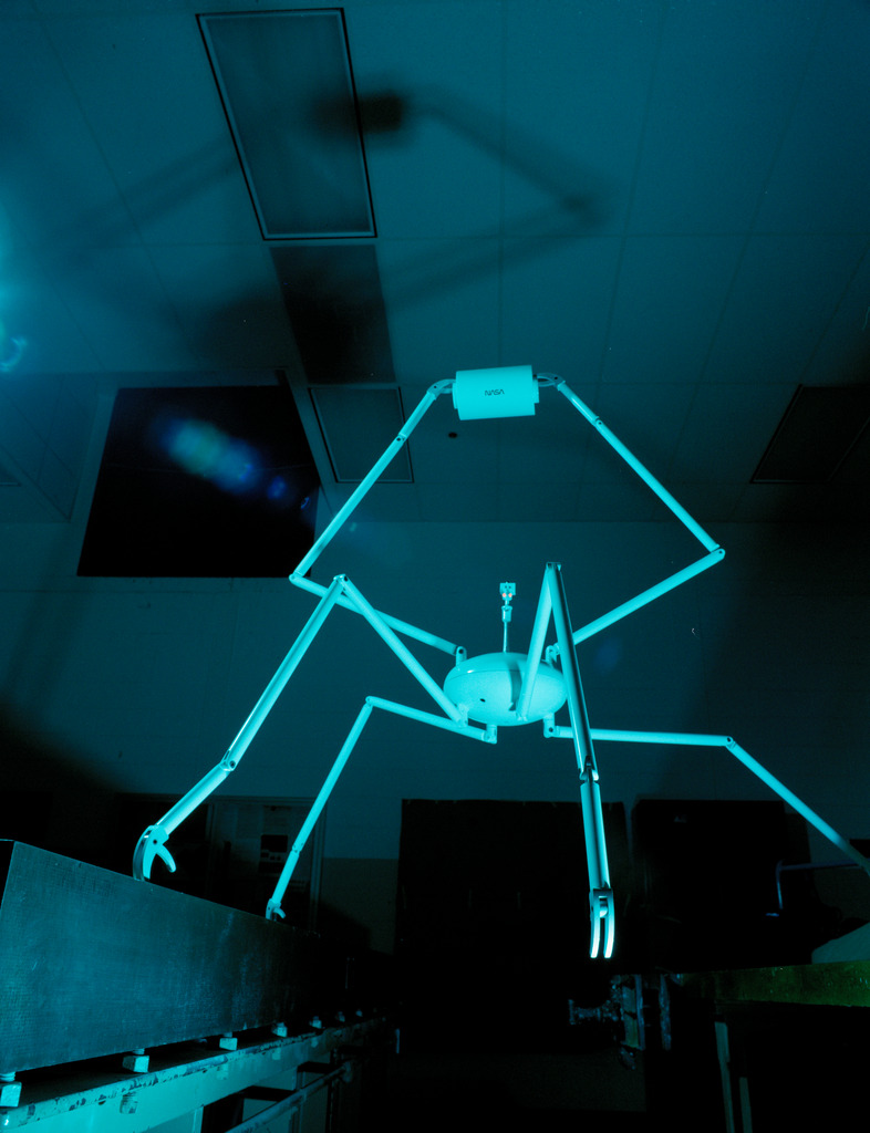 A white spider-like robot casts an eerie shadow on the ceiling.