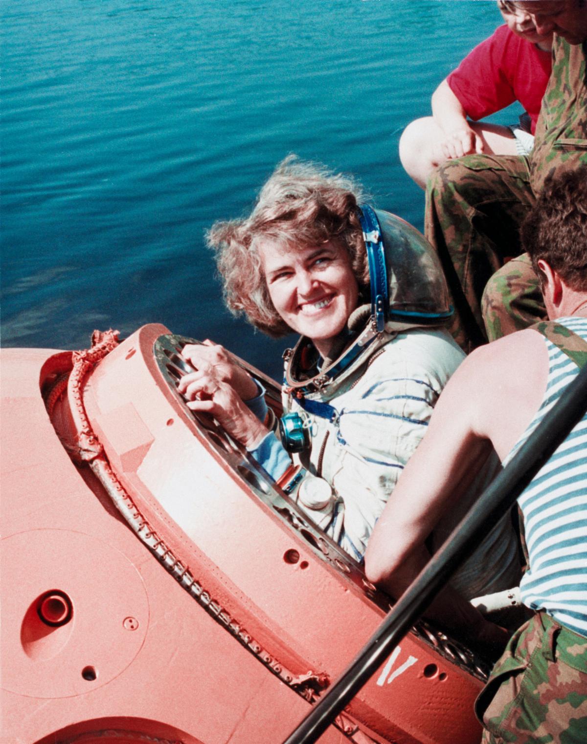 Shannon Lucid emergences from the hatch of a training version of a Soyuz spacecraft in the water.