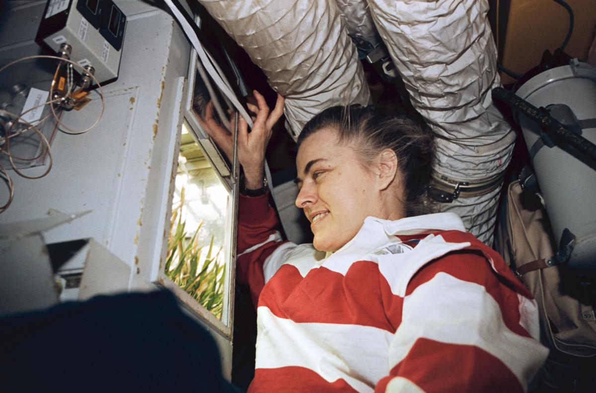 Shannon Lucid looks at plants growing in a small greenhouse enclosure aboard Mir.