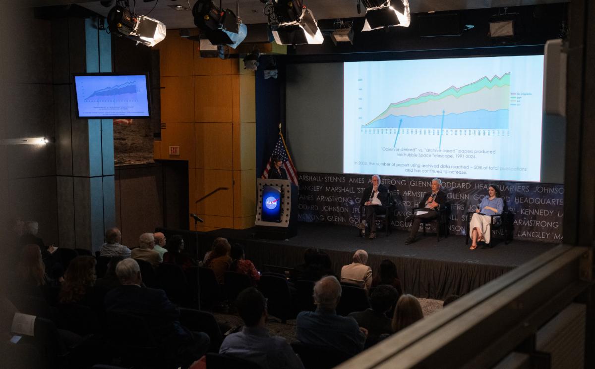 View of the stage at the Hubble Symposium during its first session. On the screen is a graph showing the number of papers written with observer-derived vs. archive-based data.