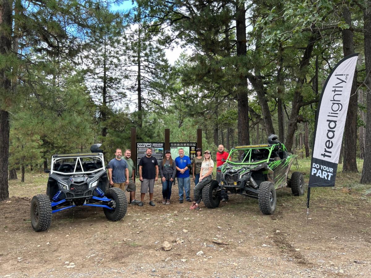 A group of people standing next to off highway vehicles and a new education kiosk.
