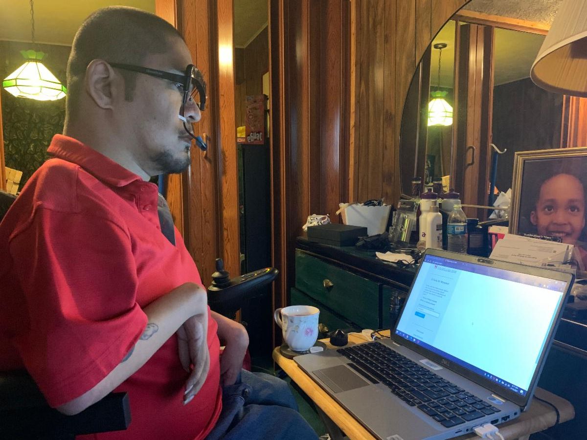 Gentleman using a computer with an oral mouse/clicker instead of a traditional hand mouse. 