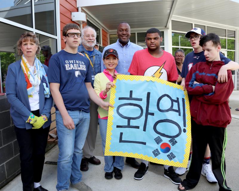 Group holds sign in Korean that says _Welcome_ 