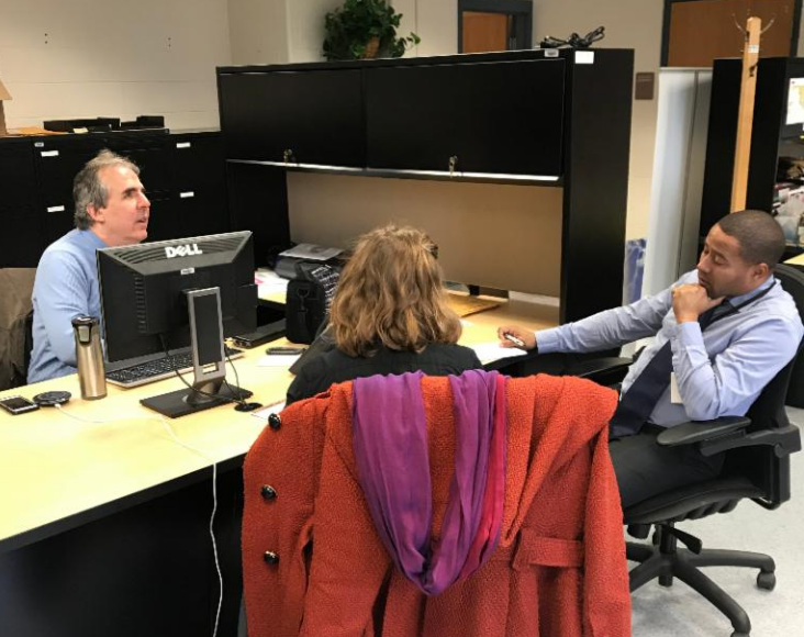 Three people sit around desk working together.