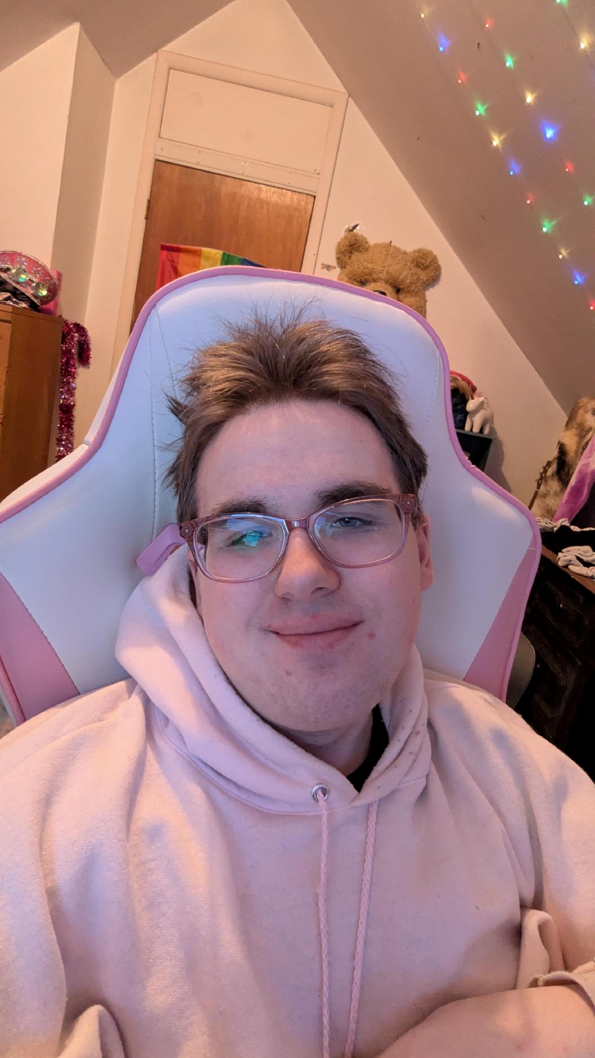 A young man with glasses smiles at the camera. There are festive lights strung up behind him. 