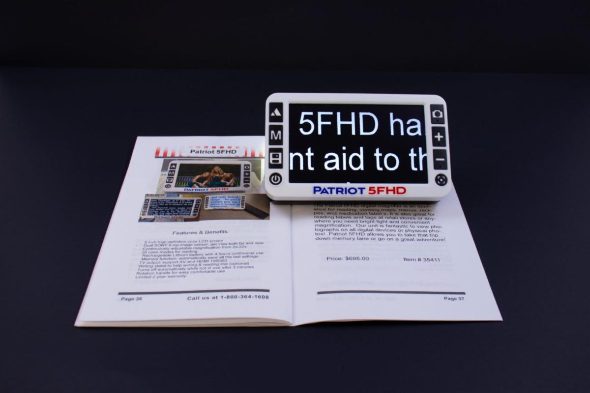 An electronic magnifier sits on top of an open manual, magnifying the text