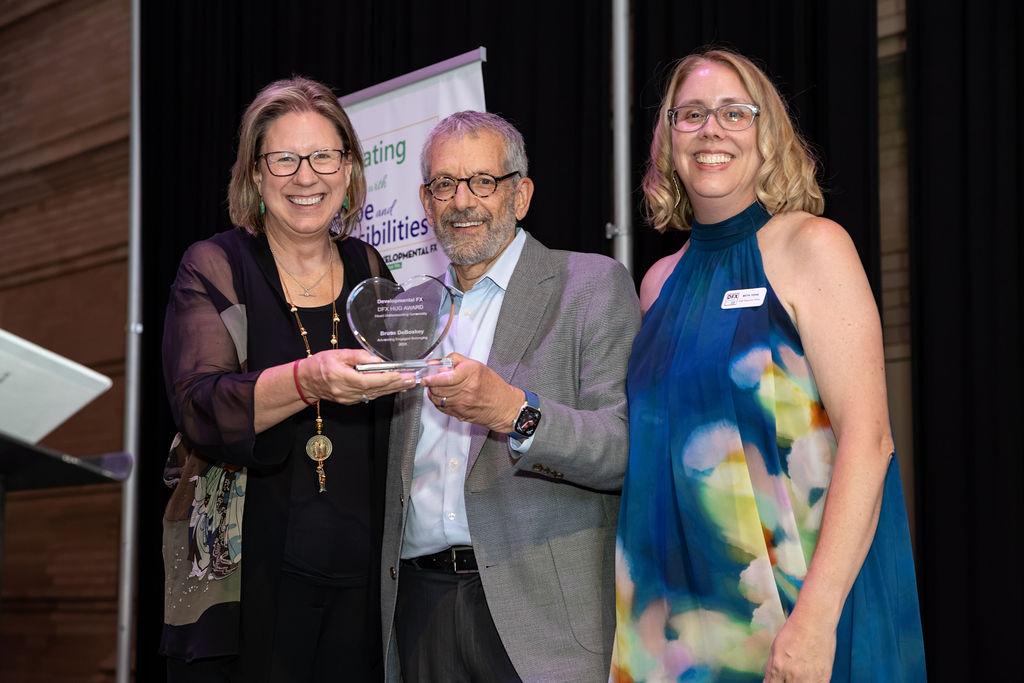 Two women presenting an award to a man 
