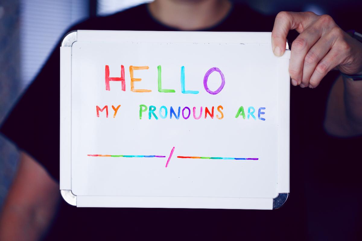 W person's hands holding up a white board that says Hello My Pronouns Are in rainbow letters Photo by Alexander Grey on Unsplash