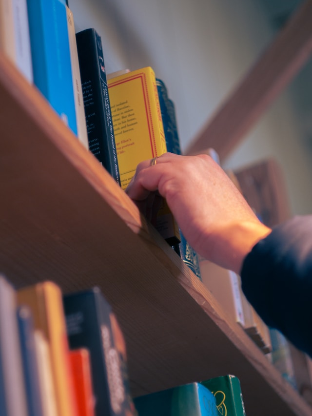 A person's hand reaching for a book on a shelf