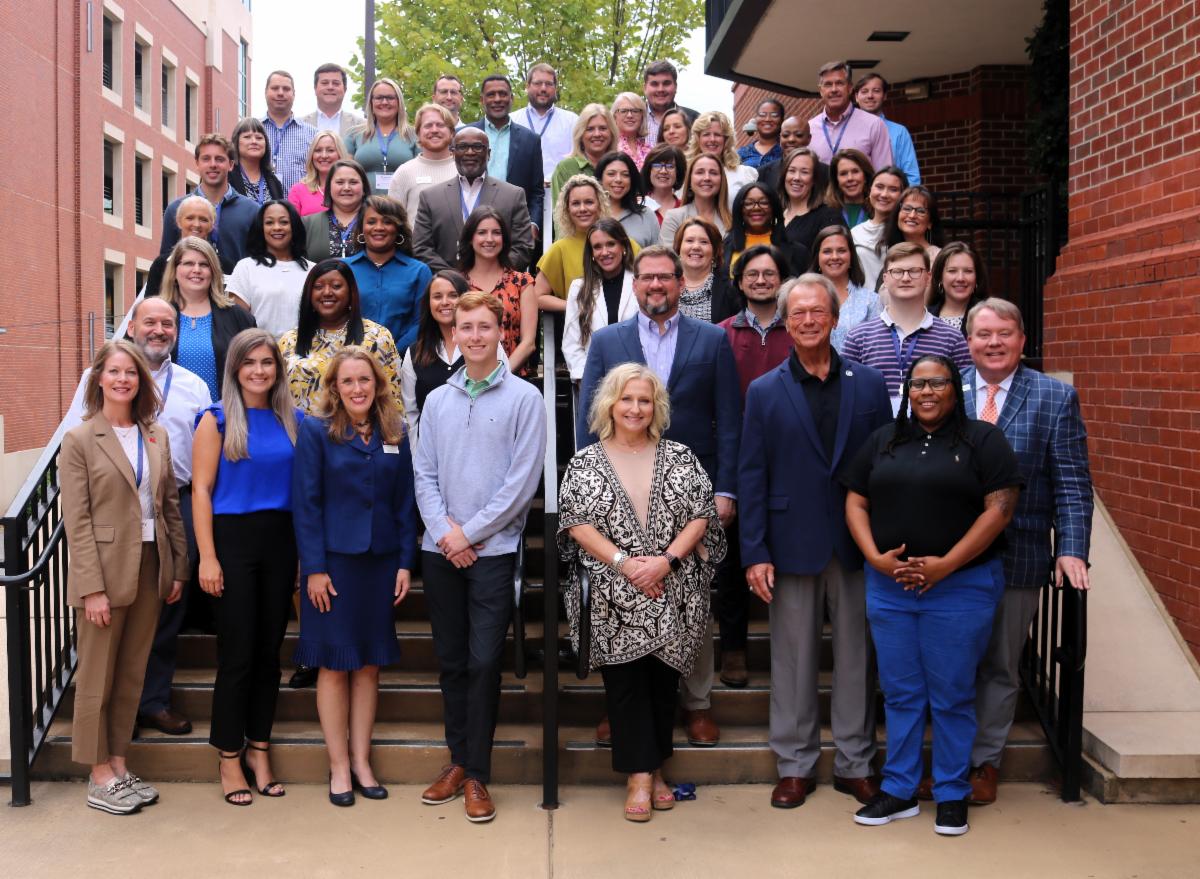 The 2024 graduating class of the Intensive Economic Development Training Course at Auburn University pose for a photo on stairs outside the Auburn University Hotel.
