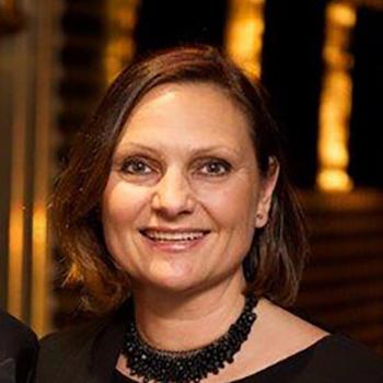 A photograph of a smiling woman with shoulder-length brown hair and a black necklace.