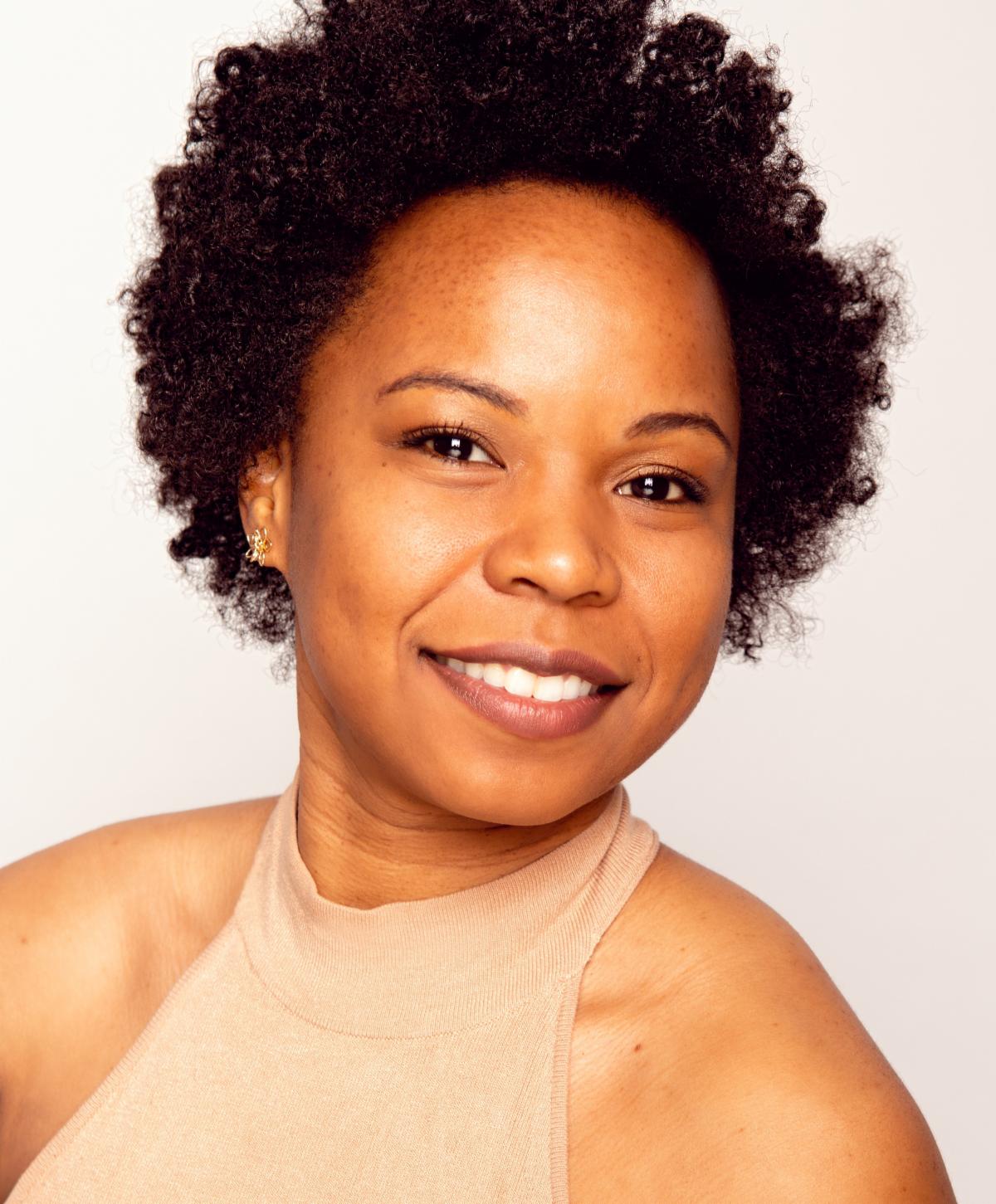 Camille Moten Rennie, professional dancer, smiling in a tan high-neck sleeveless top against a neutral light beige background