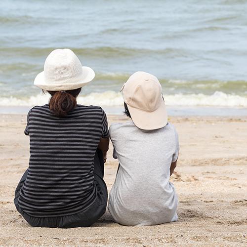 parent and kid sitting on the beach watching the water