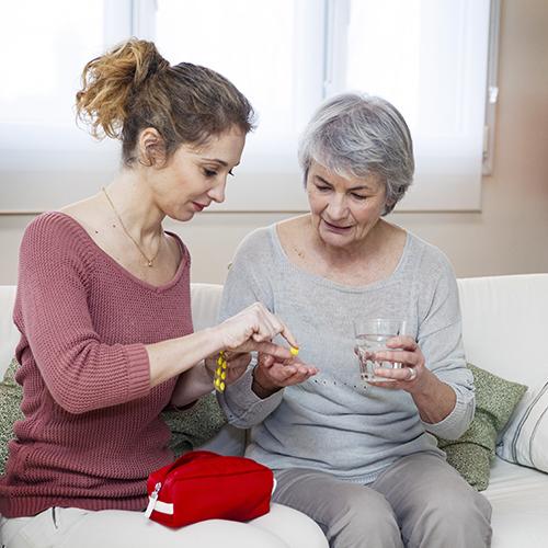 adult sitting with elderly mother and helping sort out medication