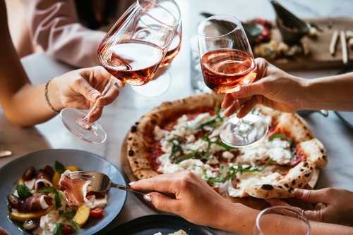 Friends enjoy a dinner party with pizza and rose wine in a bar or a restaurant.