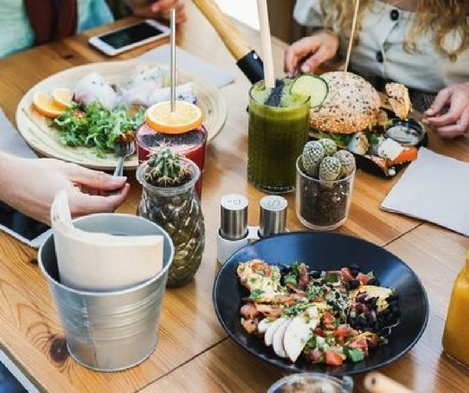 Hands view of young people eating brunch and drinking smoothies in healthy bar restaurant - Focus on left hand