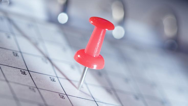 Calendar in the background with a red bulletin board pin on a day.