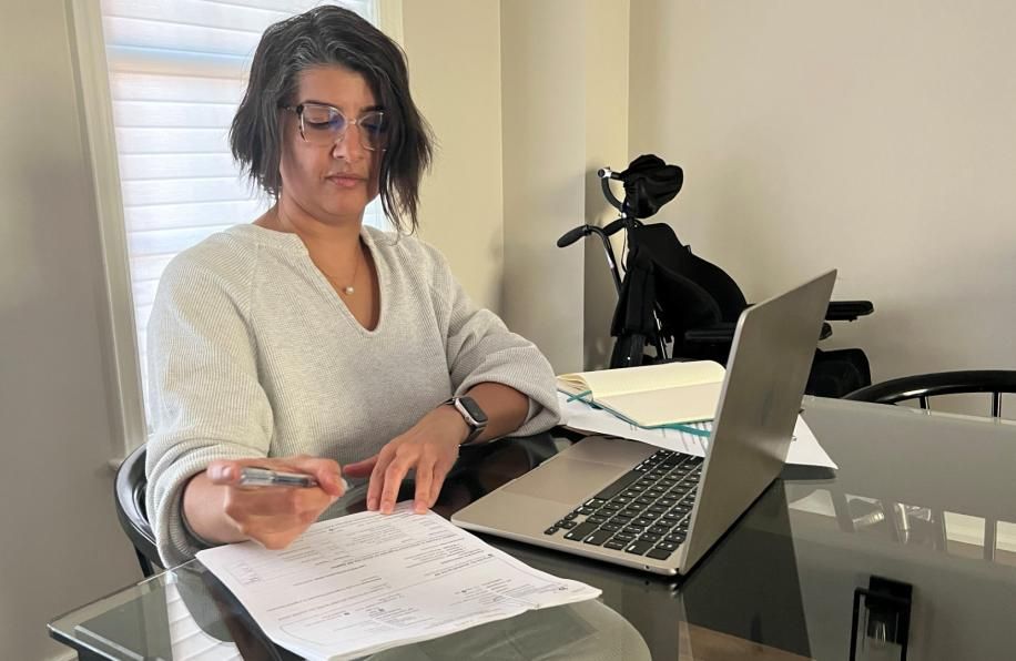 Woman with dark hair sits in front of laptop looking at papers