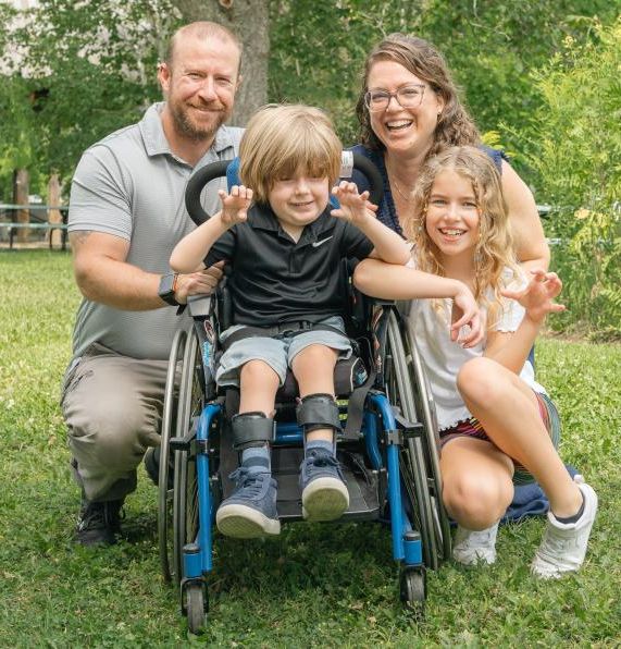 Young boy in wheelchair outside with girl and man and woman encircling him