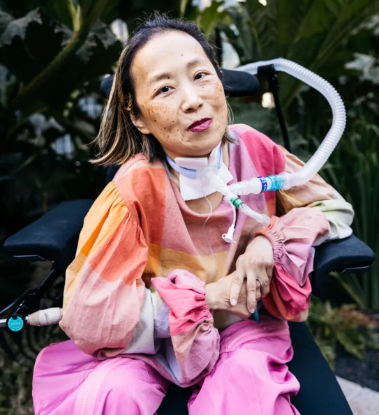 Woman in bright pink and orange with a breathing tube smiles