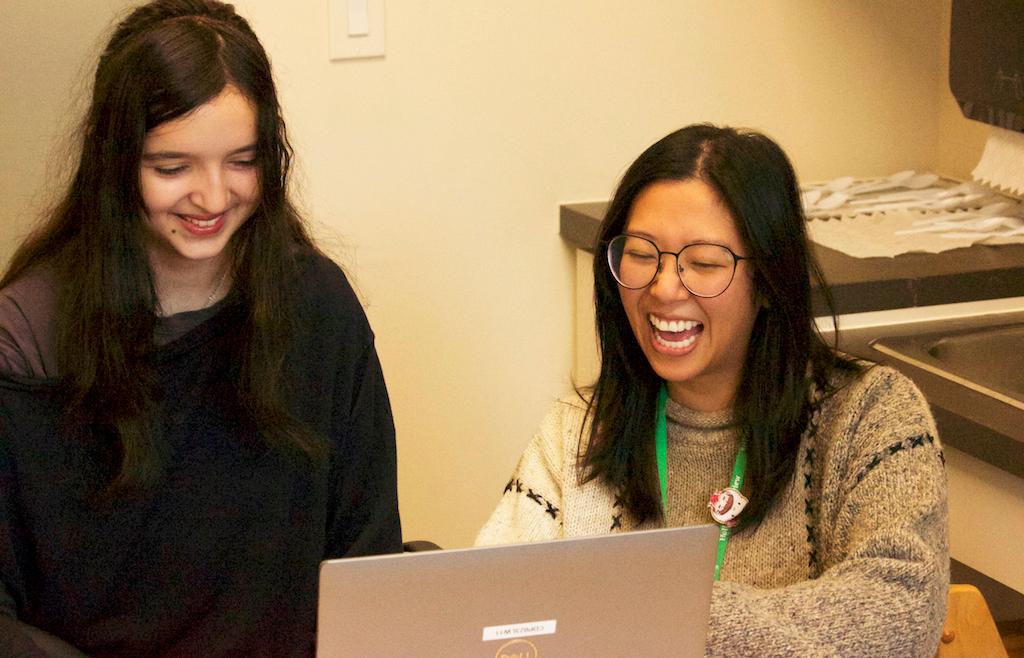 Two women laugh in front of computer screen